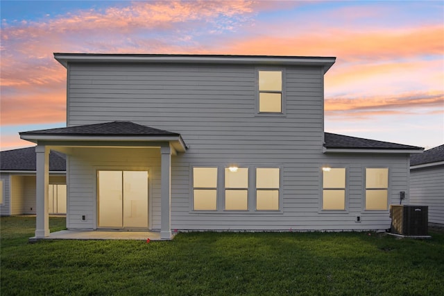 back house at dusk with central air condition unit, a yard, and a patio area