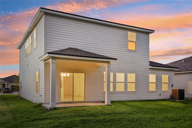 back house at dusk featuring central air condition unit, a lawn, and a patio area