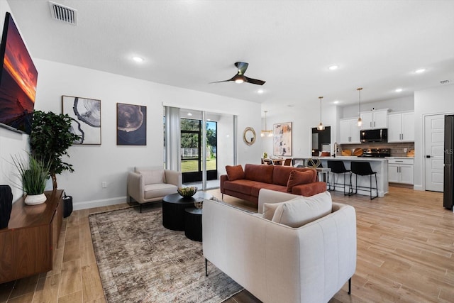 living room featuring ceiling fan, light wood-type flooring, and sink