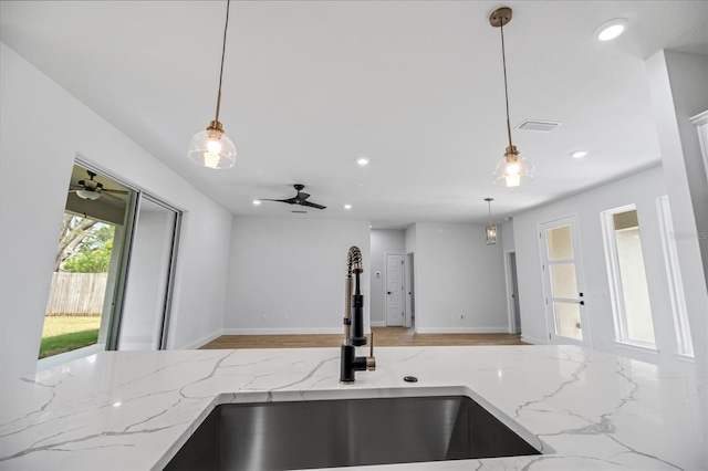 kitchen featuring hanging light fixtures, open floor plan, light stone counters, and a sink