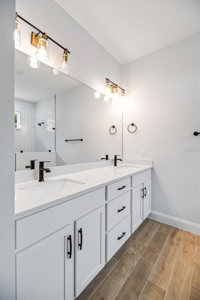 full bathroom with double vanity, a sink, tiled shower, and wood tiled floor