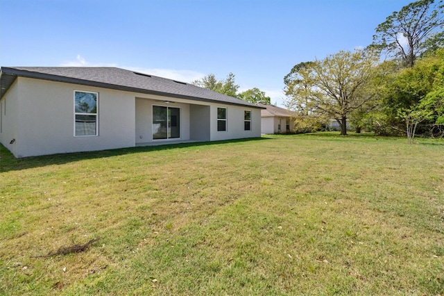 rear view of house with stucco siding, roof with shingles, and a yard