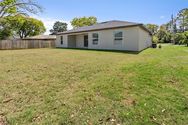 rear view of property with a lawn, stucco siding, fence, and central AC
