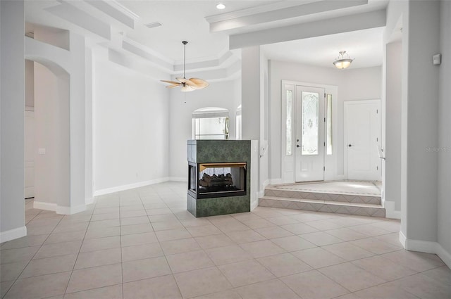 entryway with a fireplace, light tile patterned floors, ceiling fan, and ornamental molding