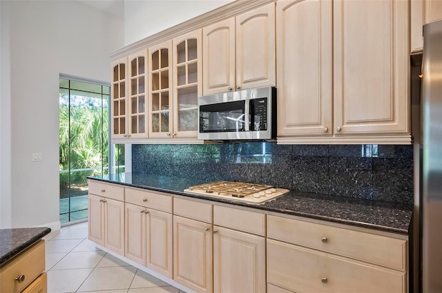 kitchen with decorative backsplash, appliances with stainless steel finishes, dark stone counters, and light tile patterned flooring