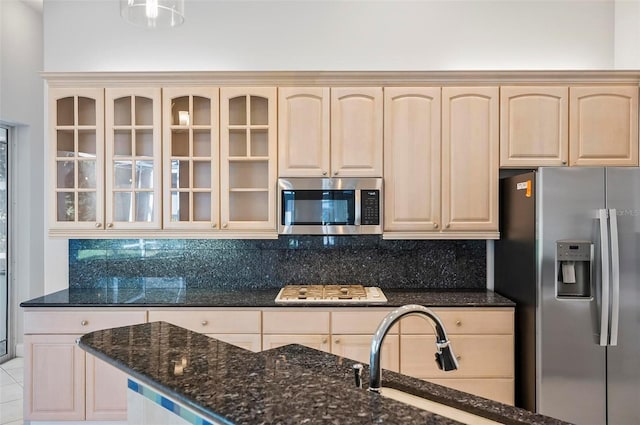 kitchen with backsplash, dark stone countertops, light tile patterned floors, light brown cabinetry, and stainless steel appliances