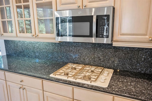 kitchen with dark stone countertops, decorative backsplash, and white gas stovetop