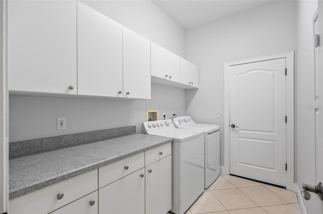 clothes washing area with cabinets, light tile patterned floors, and washing machine and clothes dryer