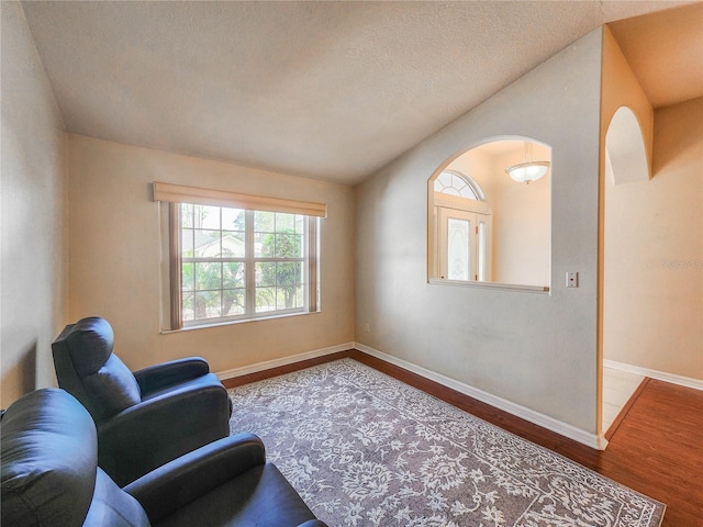 sitting room with wood-type flooring, a textured ceiling, and vaulted ceiling