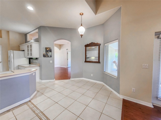 kitchen with decorative light fixtures, white fridge, white cabinetry, and light tile patterned flooring