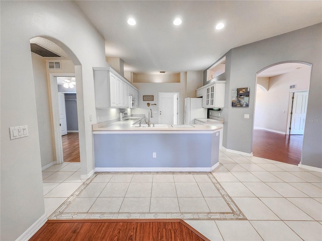 kitchen featuring kitchen peninsula, light wood-type flooring, sink, white refrigerator, and white cabinetry