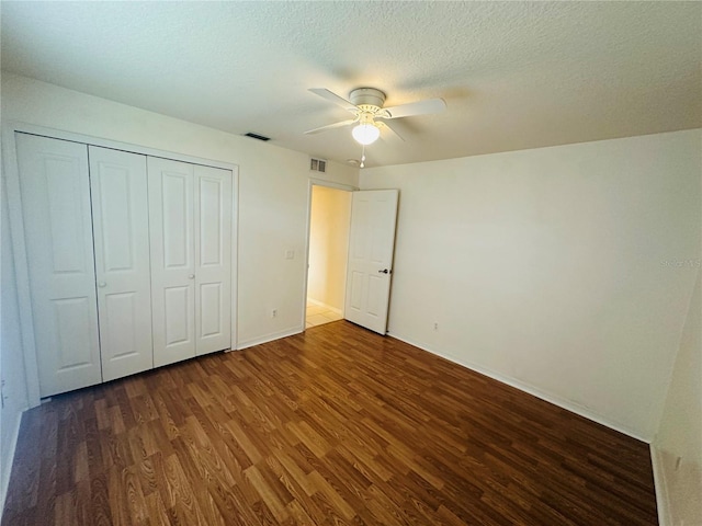 unfurnished bedroom with a textured ceiling, ceiling fan, dark wood-type flooring, and a closet