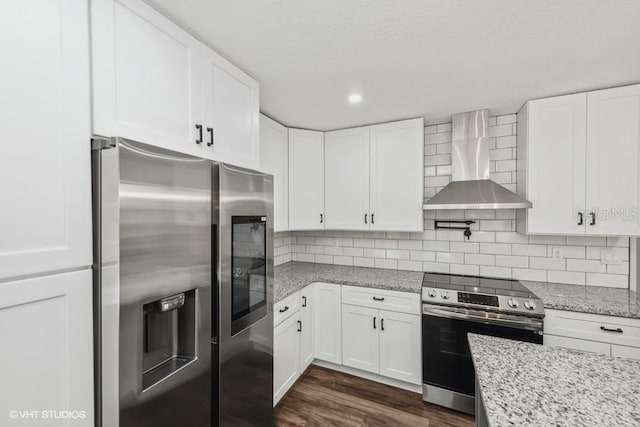 kitchen with white cabinets, wall chimney range hood, light stone countertops, appliances with stainless steel finishes, and dark hardwood / wood-style flooring