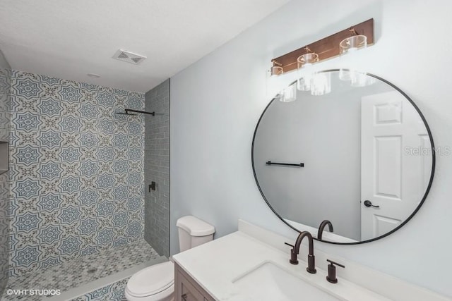 bathroom featuring a tile shower, vanity, and toilet