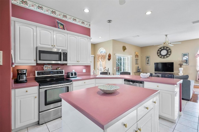 kitchen featuring kitchen peninsula, appliances with stainless steel finishes, sink, white cabinets, and a center island