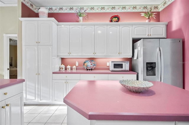 kitchen with stainless steel fridge, white cabinets, light tile patterned floors, and a kitchen island