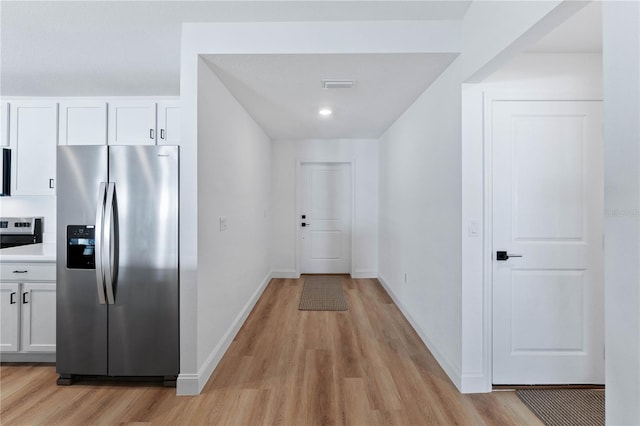 kitchen with stainless steel fridge, white cabinets, light hardwood / wood-style floors, and range