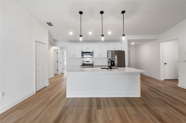 kitchen with hanging light fixtures, stainless steel appliances, a center island with sink, white cabinets, and light wood-type flooring