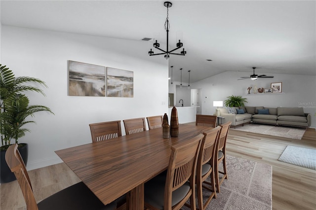 dining space featuring ceiling fan with notable chandelier, light hardwood / wood-style floors, lofted ceiling, and sink