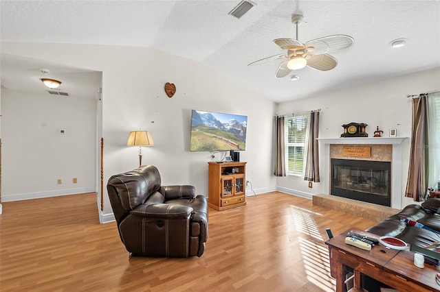 living room featuring lofted ceiling, light hardwood / wood-style flooring, ceiling fan, a textured ceiling, and a tiled fireplace