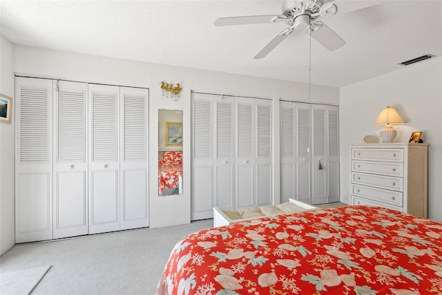 carpeted bedroom featuring a textured ceiling, two closets, and ceiling fan