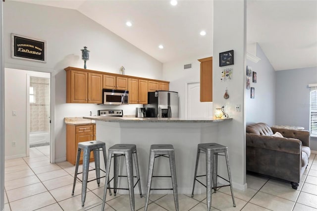 kitchen with appliances with stainless steel finishes, a kitchen breakfast bar, kitchen peninsula, and vaulted ceiling