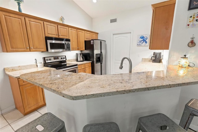 kitchen featuring light tile patterned floors, a breakfast bar area, appliances with stainless steel finishes, light stone counters, and kitchen peninsula