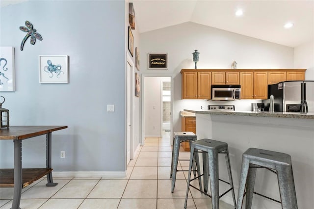 kitchen featuring lofted ceiling, light tile patterned floors, a breakfast bar area, stainless steel appliances, and light stone countertops