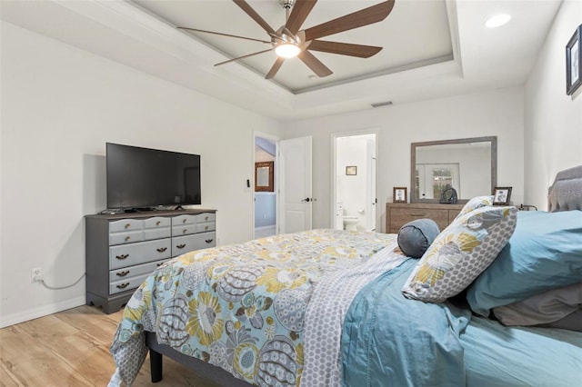 bedroom with ceiling fan, ensuite bathroom, a tray ceiling, and light hardwood / wood-style flooring