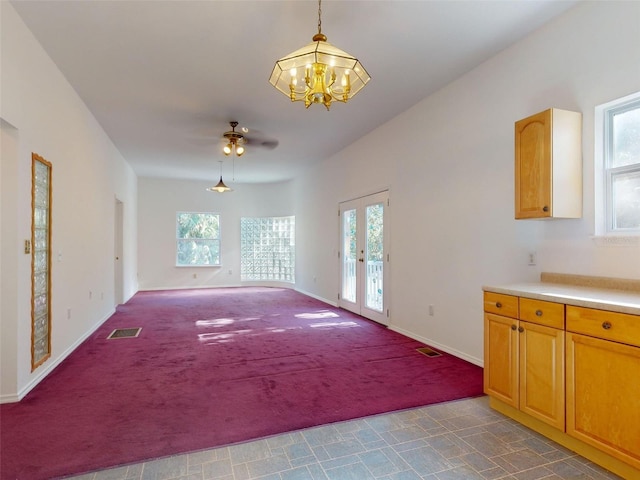 unfurnished living room featuring french doors, ceiling fan with notable chandelier, light colored carpet, and a healthy amount of sunlight