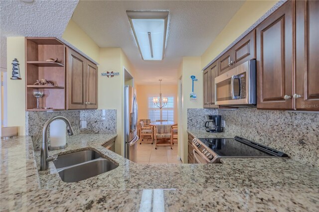 kitchen with backsplash, sink, light stone countertops, decorative light fixtures, and stainless steel appliances