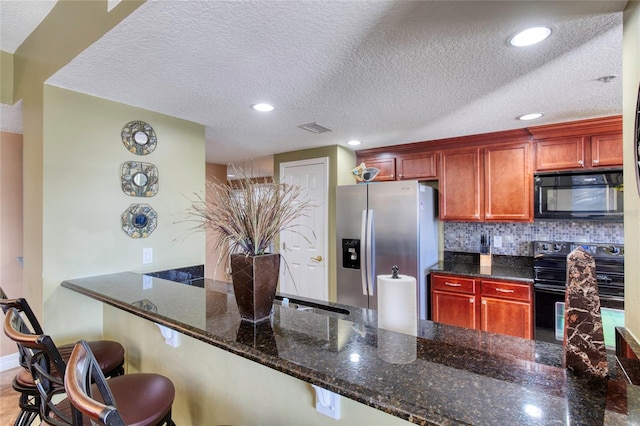 kitchen featuring black appliances, a breakfast bar, a textured ceiling, and dark stone counters