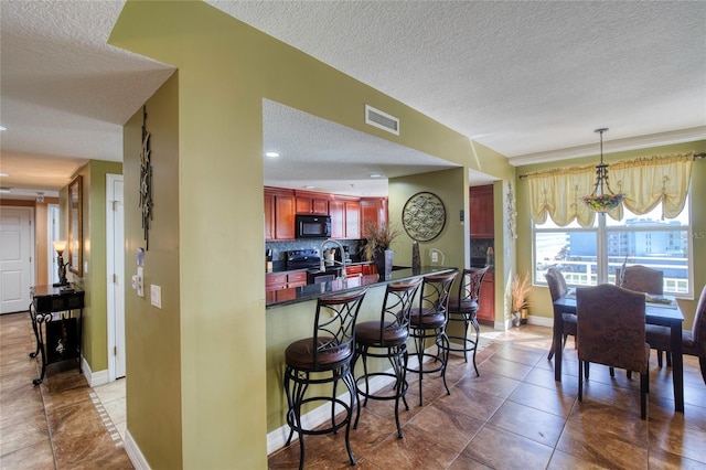 kitchen featuring a kitchen bar, kitchen peninsula, tasteful backsplash, a textured ceiling, and tile patterned flooring