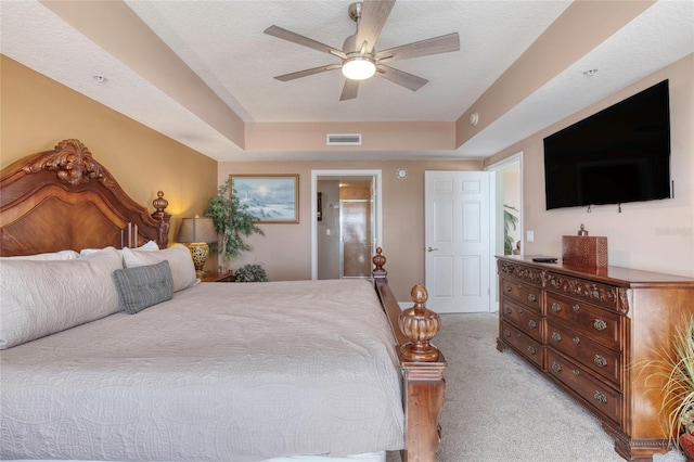 carpeted bedroom with a tray ceiling, ceiling fan, and a textured ceiling