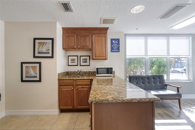 kitchen with light tile patterned flooring, a textured ceiling, light stone counters, and sink