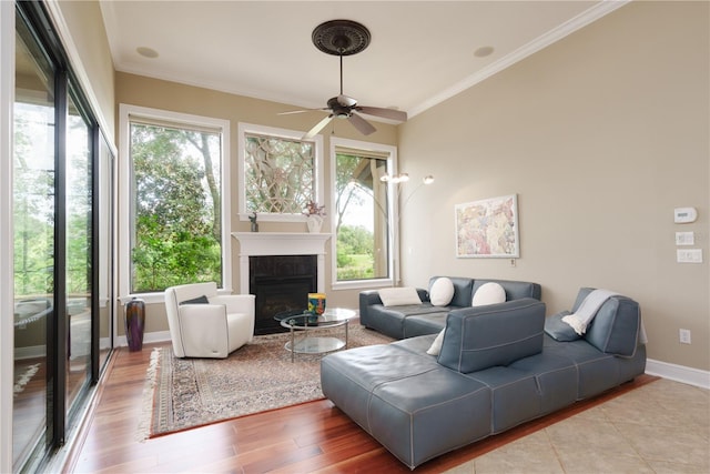 living room with ornamental molding, a glass covered fireplace, baseboards, and wood finished floors