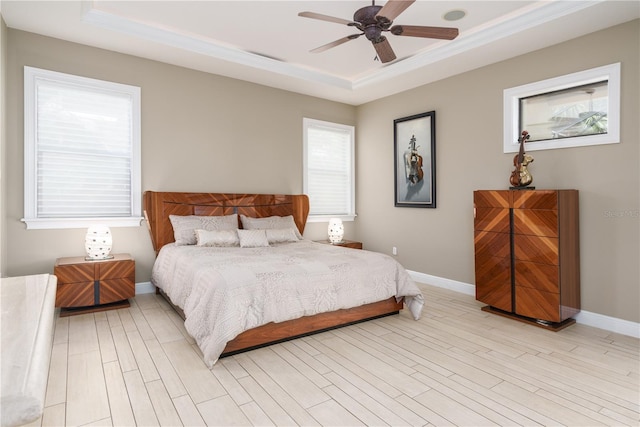 bedroom with light wood-type flooring, a raised ceiling, a ceiling fan, and baseboards