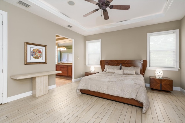 bedroom featuring light wood-type flooring, a tray ceiling, visible vents, and baseboards