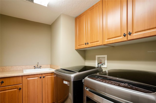 washroom with cabinet space, a textured ceiling, separate washer and dryer, and a sink