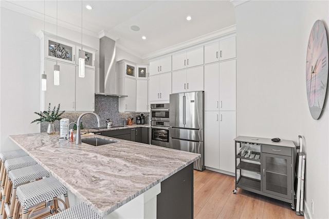 kitchen featuring sink, wall chimney range hood, kitchen peninsula, white cabinets, and appliances with stainless steel finishes