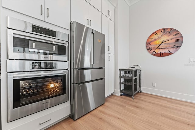 kitchen with white cabinets, appliances with stainless steel finishes, and light hardwood / wood-style flooring