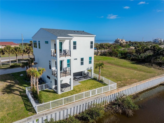 back of property featuring a patio area, a balcony, a yard, and a water view