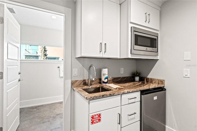 kitchen featuring stainless steel microwave, dark stone countertops, white cabinetry, and sink