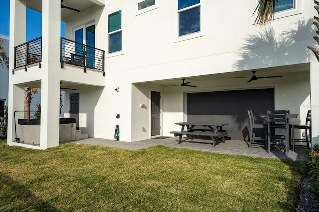 back of property with a balcony, ceiling fan, a patio area, a hot tub, and a lawn