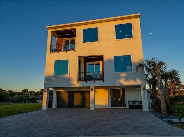 back house at dusk featuring a balcony and a garage