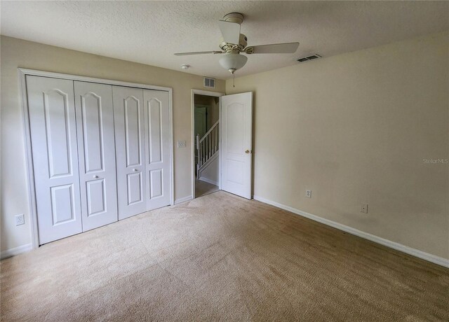 unfurnished bedroom with a textured ceiling, light colored carpet, a closet, and ceiling fan