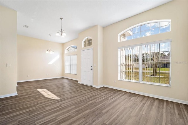 interior space with dark hardwood / wood-style flooring, a notable chandelier, plenty of natural light, and a high ceiling