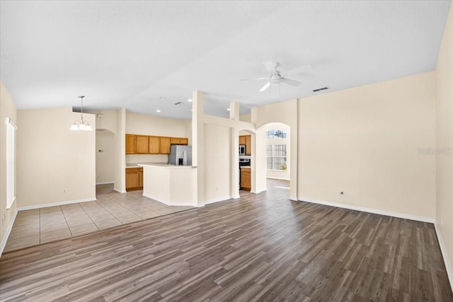 unfurnished living room featuring lofted ceiling, ceiling fan with notable chandelier, and light wood-type flooring