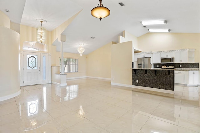 tiled entryway with ornate columns, high vaulted ceiling, and a chandelier