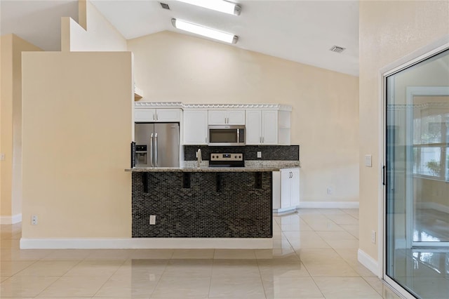 kitchen featuring white cabinetry, vaulted ceiling, a breakfast bar, light tile patterned flooring, and appliances with stainless steel finishes